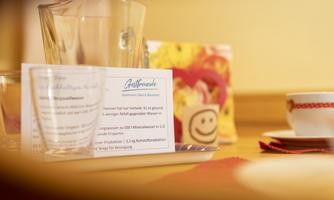 A table setting with a water jug and a menu. In the background, a cup and a cheerful decoration can be seen.