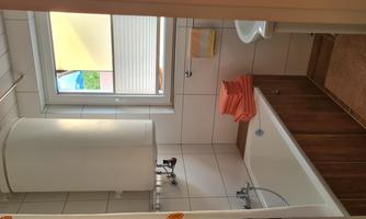 A modern bathroom with a bathtub, a sink, and a large window. Orange towels are neatly stacked.