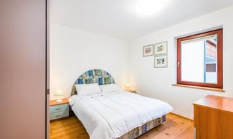 A bright bedroom with a comfortable double bed and wooden floor. There are two nightstands and a large window overlooking the outside.