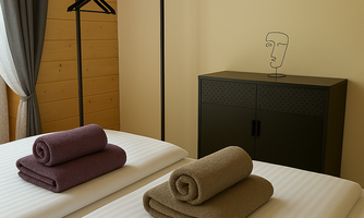 A bright room with two beds and fresh towels. A decorative sculpture and a clothing rack complement the furnishings.