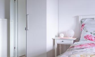 White wardrobe with mirror door and bedside table next to the bed – here clothes and personal items find their place, everything appears bright and tidy.