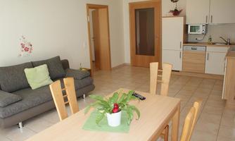 A modern living room with a gray couch and a wooden table. The kitchen is open and well-equipped.