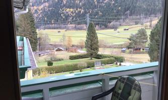 A beautiful balcony view of a green meadow landscape and mountains in the background. A chair is ready for relaxation.
