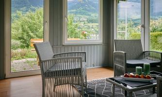 A cozy room with two chairs and a table. Through the windows, you can see the green landscape and mountains.