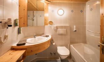 A modern bathroom with wooden details. It features a bathtub, a sink, and a toilet.