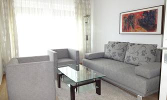 A modern living room with gray sofas and a glass table. The windows let in plenty of light and create a bright atmosphere.