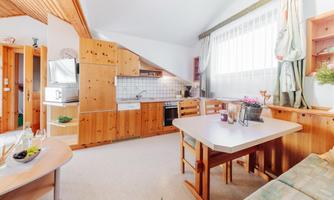 A cozy kitchen with wooden paneling and a dining table. Large windows provide plenty of daylight.