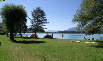 A green meadow by the shore of a clear lake. People are relaxing and enjoying nature.