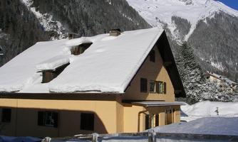 A cozy house in the snow with a snow-covered roof. In the background, snow-covered mountains can be seen.