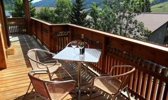 A cozy balcony with a table and four chairs. In the background, green hills and trees can be seen.