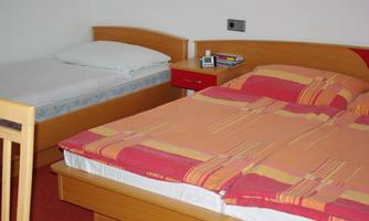 A simple bedroom with two beds. One of the beds is made up, the other has only a mattress and a pillow.