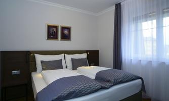A cozy bedroom with two beds and elegant bedding. The windows are equipped with light curtains and there are pictures hanging on the wall.
