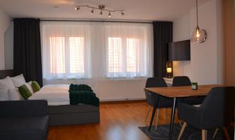 A modern room with a cozy bed, a dining table, and elegant chairs. Large windows provide plenty of daylight.