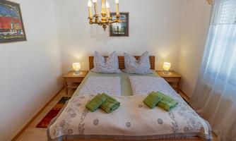 A cozy bedroom with a double bed and two nightstands. It features light walls, a wooden ceiling, and decorative lights.