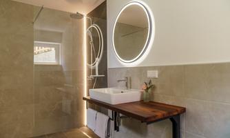 A modern bathroom with gray tiles and a large round mirror. The wooden sink table adds an elegant touch to the space.