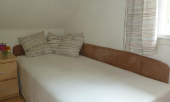 A cozy room with a single bed and striped pillows. Next to the bed is a nightstand with a vase full of flowers.