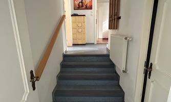 A bright hallway with a staircase leading upwards. There are doors and a picture on the walls.
