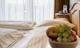 A cozy bedroom with two beds and bright bedding. On the bedside table, there is a bowl of fresh fruit.