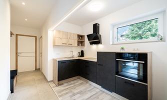 A modern kitchen with black and light wooden furniture. The room has plenty of natural light and a view of the garden.