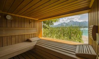 A cozy sauna with wooden interiors and a view of a picturesque landscape. In the background, mountains and a clear sky can be seen.