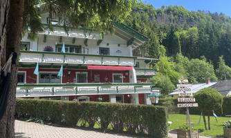 A picturesque building with several balconies and a red hue. Surrounded by green trees and well-maintained gardens.