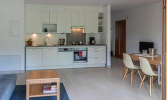 A modern kitchen with bright cabinets and modern appliances. A dining area with wooden chairs and a table is also visible.