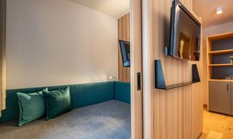 A modern room with a cozy blue sofa and a television on the wall. Next to the sofa, there is a small cabinet with shelves.