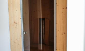 A modern infrared sauna with wooden cladding and a glass door. It is located in a bright room and offers a place for relaxation.