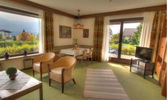 A cozy living/dining room with large windows and a beautiful view. The furnishings consist of a table, chairs, and two comfortable armchairs.
