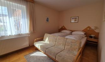 A cozy bedroom with a double bed and a seating area. Large windows provide plenty of natural light.