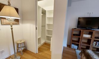 A bright room with a wardrobe, a TV, and a bookshelf. A floor lamp stands next to a small table.