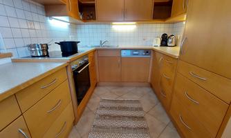 A modern kitchen with wooden furniture and tile floor. Pots and kitchen appliances are on the countertop.