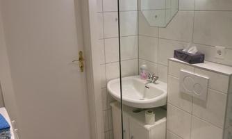 A modern bathroom with white tiles and a sink. The toilet and a mirror are also present in the room.