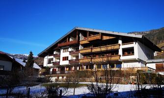 A modern building in the mountains with several balconies. The sky is clear and blue, surrounded by snow-covered land.