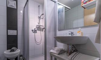 A modern bathroom with a shower, a sink, and towels. The walls are brightly tiled and the furnishings are functional.