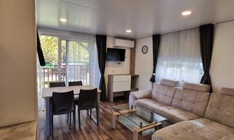 A modern living room with a comfortable sofa and a dining table. Large windows let in plenty of light and offer a view of the outdoors.