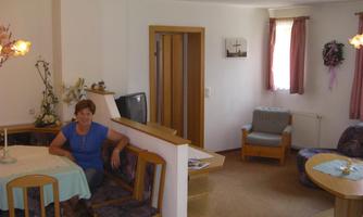 A cozy living kitchen with a table and chairs. A woman is sitting relaxed on a bench.