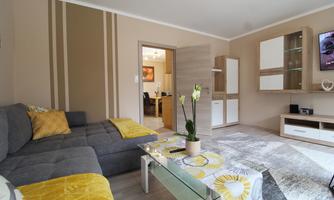 A modern living room with a gray sofa and yellow cushions. The room is bright and friendly, with a coffee table and a beautiful plant.