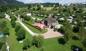 A large green space with a residential house and camping sites. Surrounded by trees and a clear landscape.