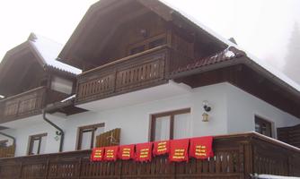 A traditional wooden house in the snow with a balcony. Red banners hang over the balcony.