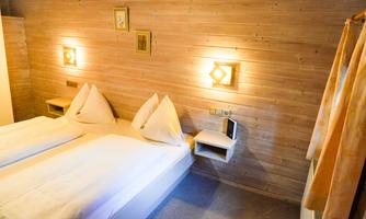 A cozy bedroom with two beds and warm wood decor. The walls are paneled with wood and warmly lit.