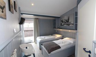 A cozy room with two beds and a modern design. There are windows with access to a balcony and a decorative wall with a picture.