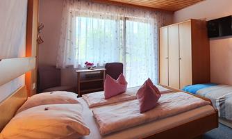 A cozy room with two beds and an extra bed. Plenty of daylight pours in through large windows.