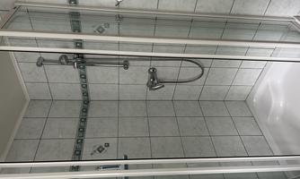 A modern shower with glass walls and gray tiles. The shower features a hand-held showerhead and a fixed showerhead.