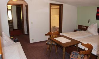 A simple hotel room with two beds, a table, and chairs. There is access to a bathroom and a pleasant atmosphere.