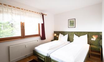 A cozy bedroom with two single beds and wooden details. Large windows provide plenty of daylight.