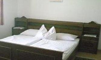 A simple bedroom with a large double bed and white bedding. A picture hangs on the wall, and there is a small nightstand.