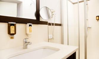 A modern bathroom with a sink, mirror, and shower cabin. The walls are bright, and the furnishings are functional and stylish.
