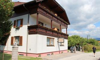 A beautiful house in typical alpine style with a decorated balcony. The garden is well-maintained and the sky is partly cloudy.