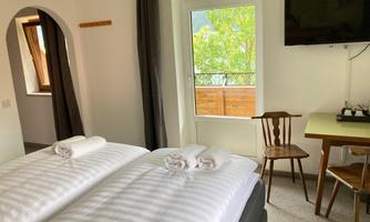 A bright and cozy hotel room with a double bed, a table, and a chair. The room has a window overlooking nature.